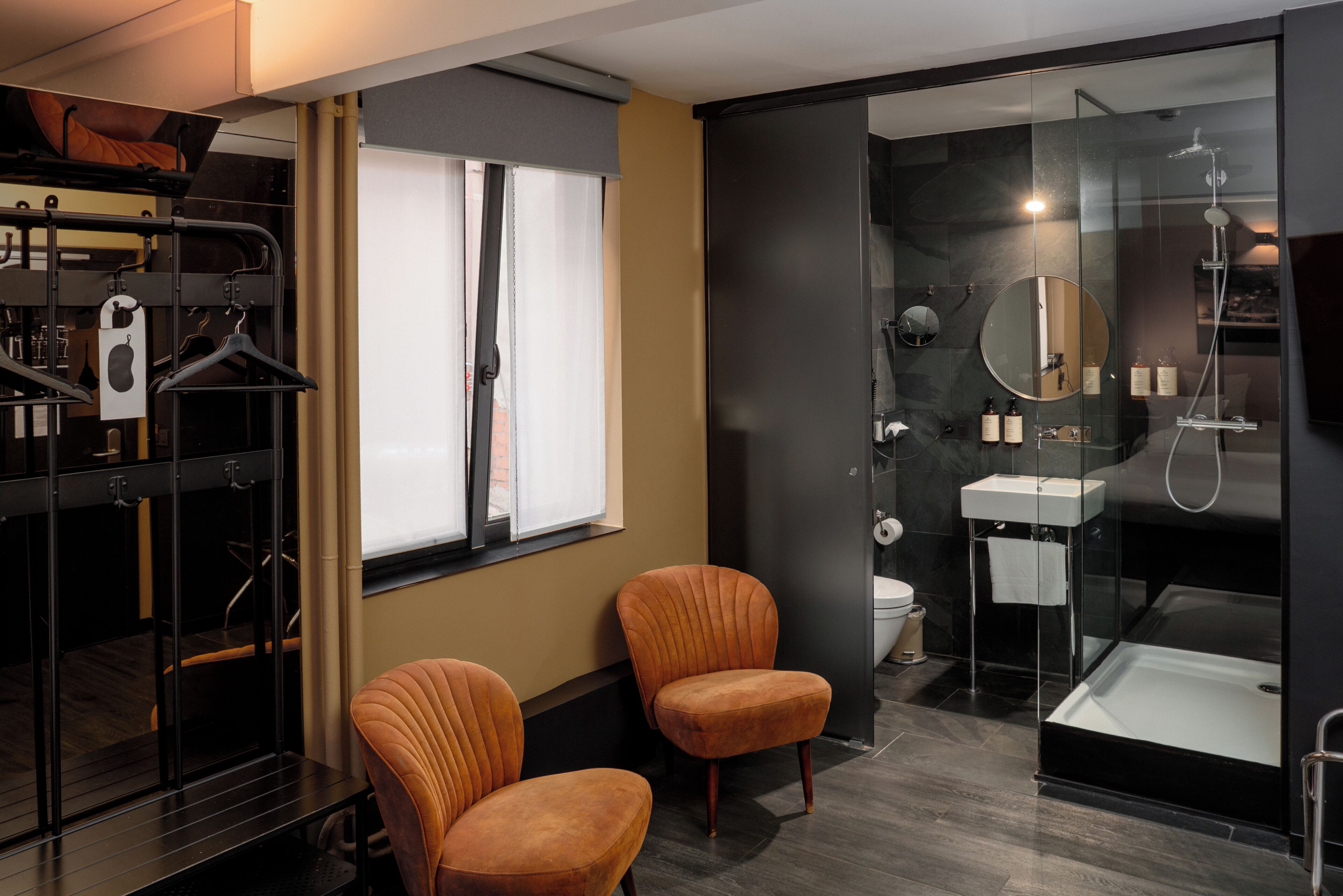 A modern bathroom with a glass shower enclosure, a sink, and two chairs.