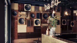A bar area with wooden paneling, multiple speakers, and a neon sign. - HotelO Kathedral Antwerp (Antwerp)