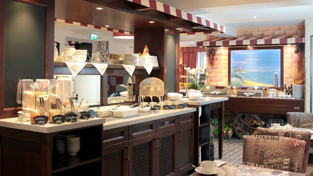 Un vestíbulo de hotel con un mostrador que exhibe productos para el desayuno, un amplio ventanal con vistas y una silla de estilo vintage.