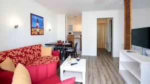 Una sala de estar con un sofá rojo, una mesa de centro blanca y un televisor sobre un mueble.