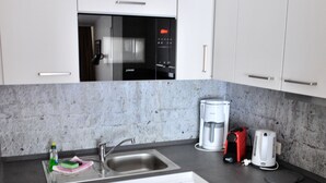 Una cocina moderna con armarios blancos, un lavamanos de acero inoxidable, microondas integrado, cafetera y estufa.