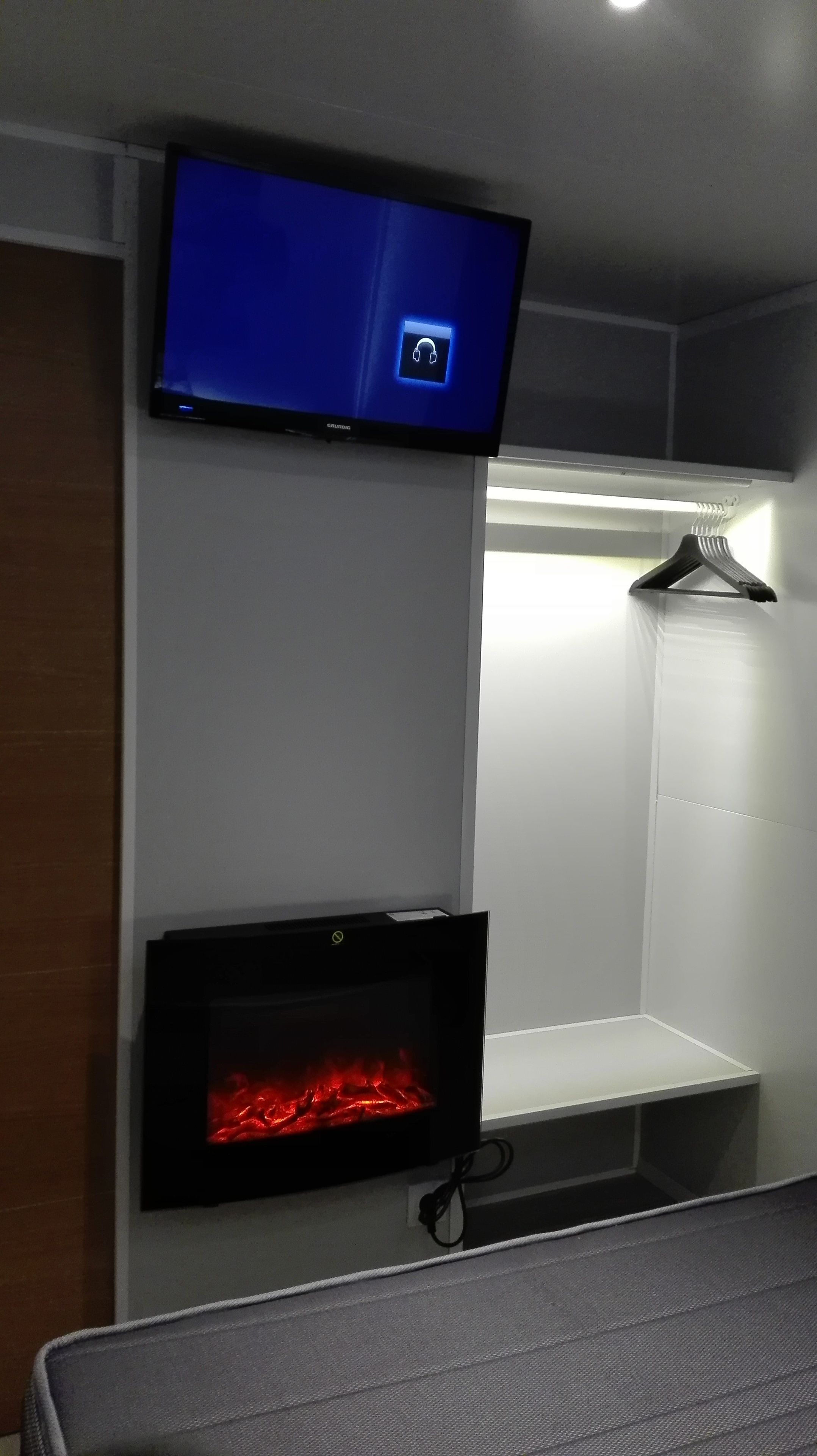 Una habitación con televisión de pantalla plana en la pared, chimenea encendida y perchero.