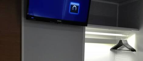 Una habitación con televisión de pantalla plana en la pared, chimenea encendida y perchero.