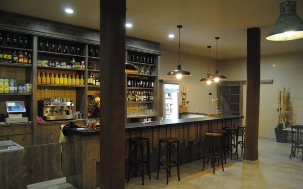 A bar area with wooden shelves stocked with bottles, a cash register, and bar stools. - Hotel Santa Bàrbara (Cercs)