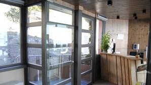 Un espace d’accueil avec un comptoir en bois, une plante en pot et de grandes fenêtres.