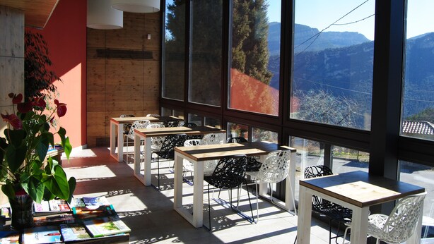 Un espace extérieur moderne aménagé avec des tables et des chaises, de grandes fenêtres offrant une vue sur les montagnes et un pot de fleurs avec des fleurs rouges.