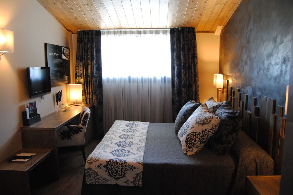 A hotel room with a bed, a desk, a chair, a TV, and a window with curtains.