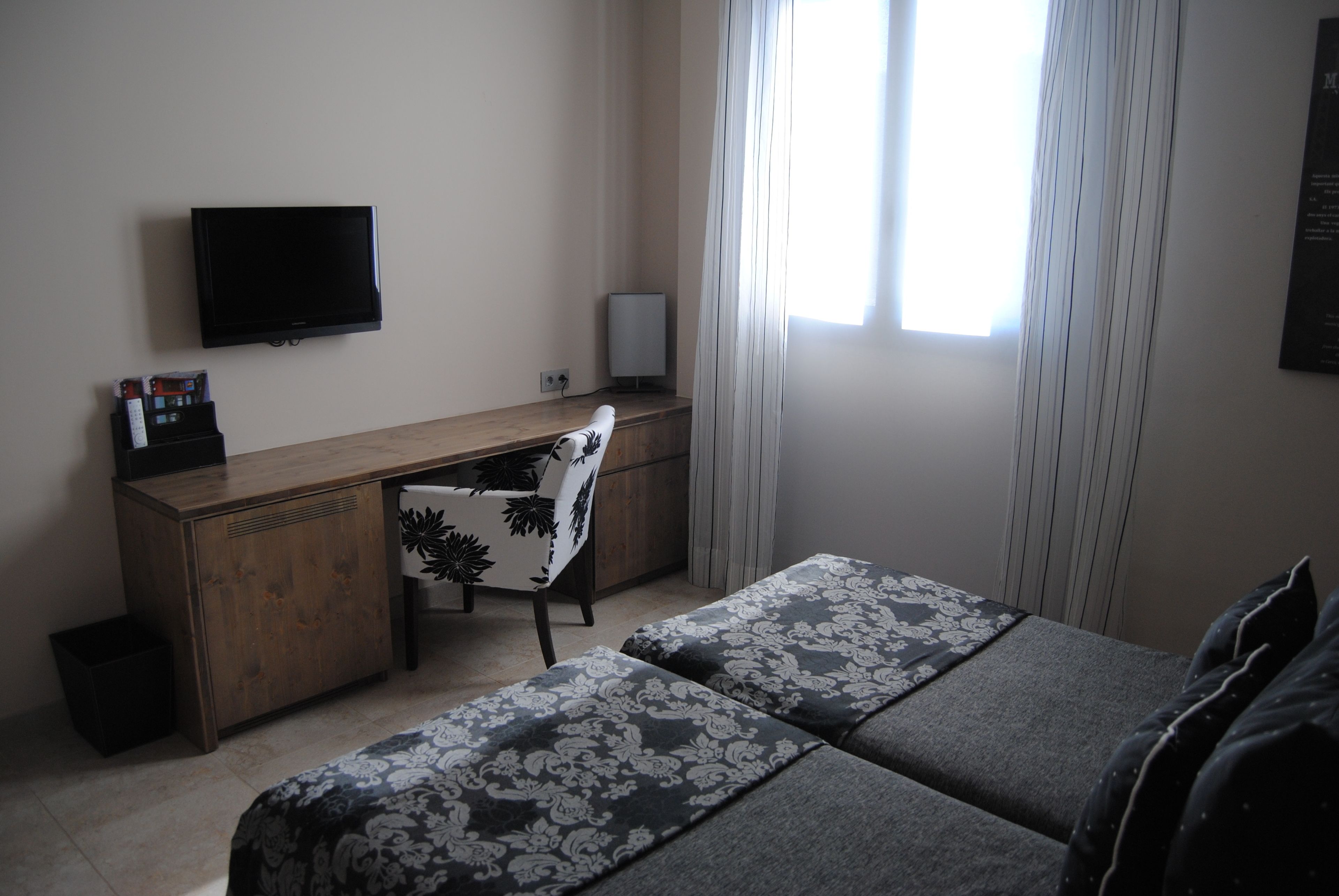Habitació d'hotel amb llit, escriptori, cadira, televisió i finestra amb cortines.