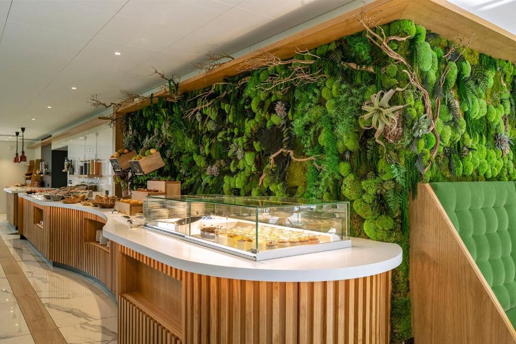 Un espace d’accueil avec un comptoir en bois, une vitrine et un mur recouvert de feuillage vert.