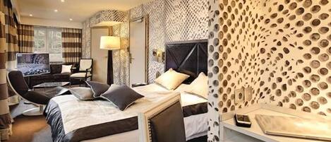 A hotel room with two beds, a desk, a chair, a TV, and a patterned wall.
