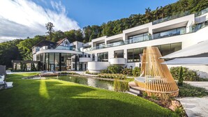 Un bâtiment moderne doté d’une structure circulaire en verre, d’une piscine et d’une terrasse en bois avec des sièges.