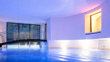 An indoor swimming pool with a glass bridge, large windows, and a warm light source.