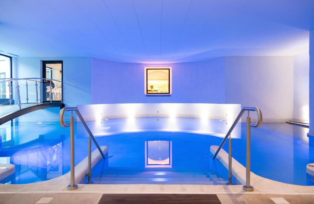 Une piscine intérieure dotée d’un mur en verre, de rampes métalliques et d’un tableau encadré accroché au mur.