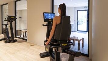 Een vrouw gebruikt een hometrainer met een digitaal scherm, in een kamer met houten vloer en een bank.