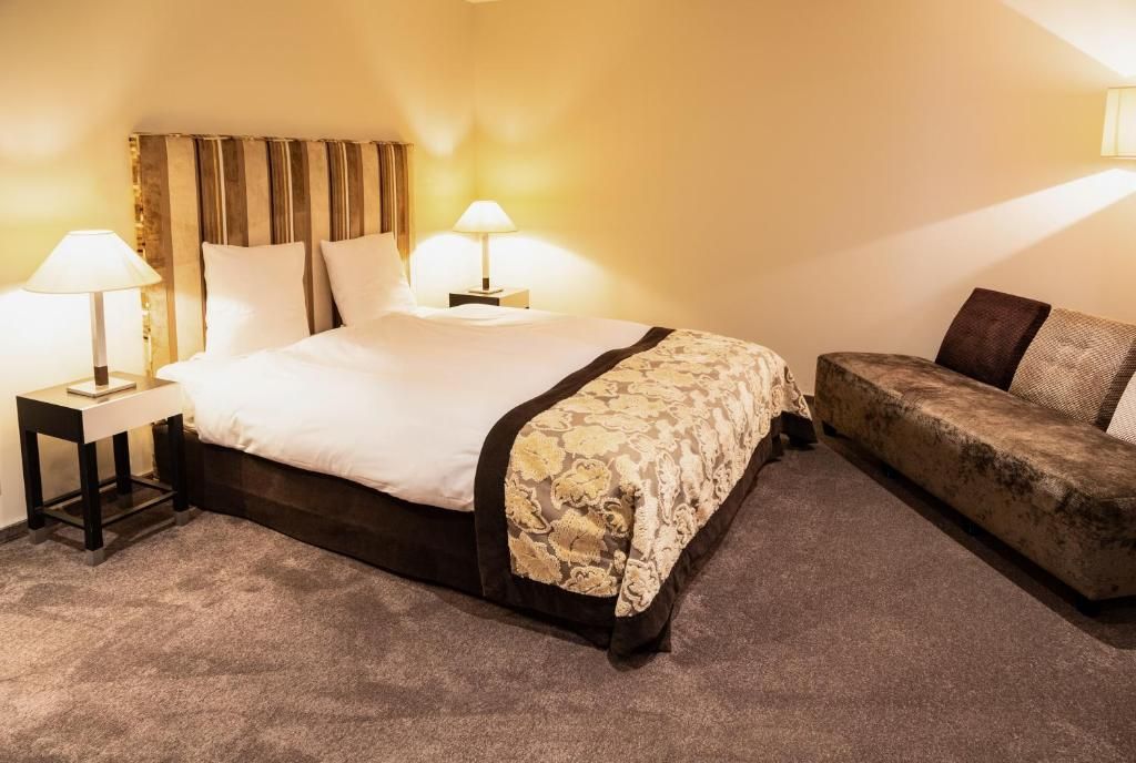 Une chambre d’hôtel avec un lit, deux lampes de chevet, un canapé et un sol recouvert de moquette.