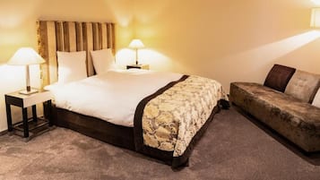 Une chambre d’hôtel avec un lit, deux lampes de chevet, un canapé et un sol recouvert de moquette.