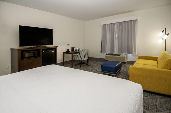 A hotel room with a bed, a television, a desk with a chair, a yellow armchair, and a window with curtains. - Hampton Inn West Monroe (Monroe)