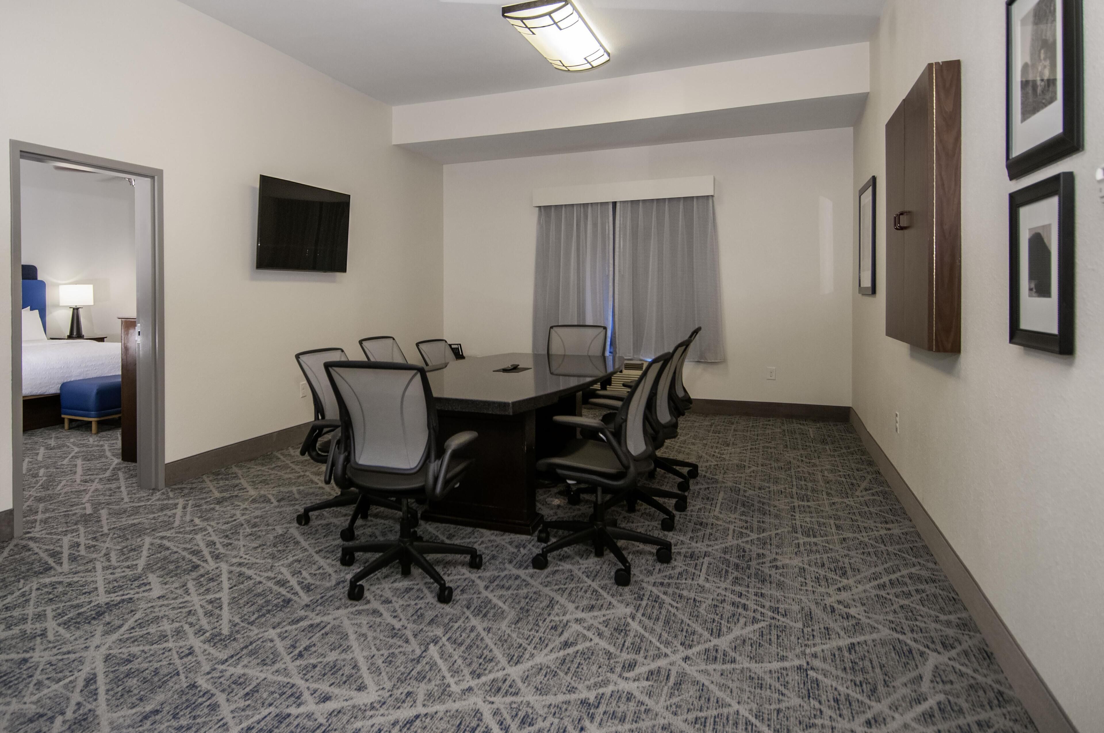 Un salón de conferencias con una mesa rectangular, seis sillas, un televisor de pantalla plana y cuadros en la pared.