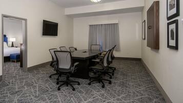Un salón de conferencias con una mesa rectangular, seis sillas, un televisor de pantalla plana y cuadros en la pared.