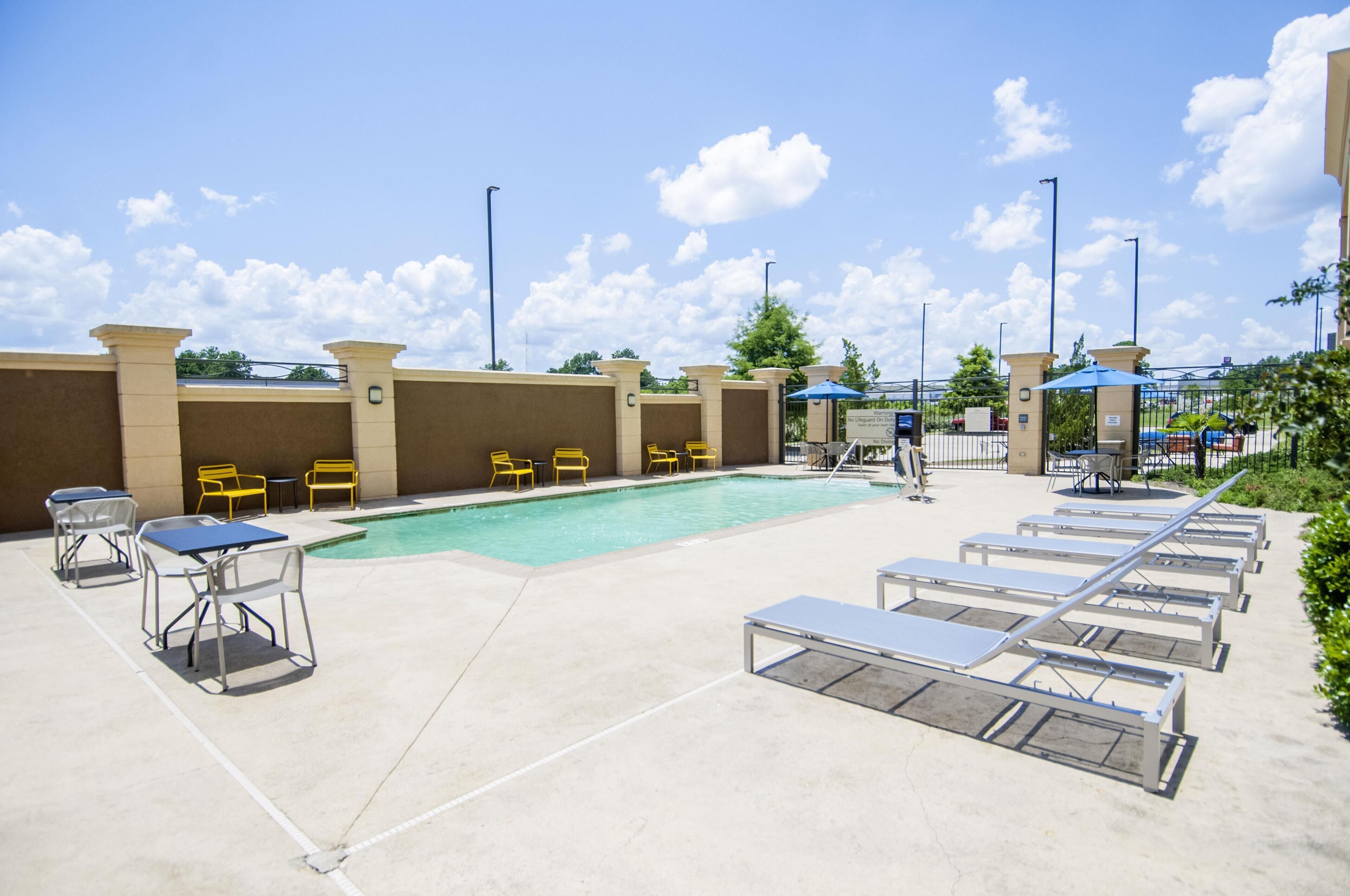 Un espace piscine avec des chaises longues et des tables, un ciel dégagé et une clôture.