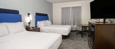 A hotel room with two beds, a desk, a television, and a window with curtains.
