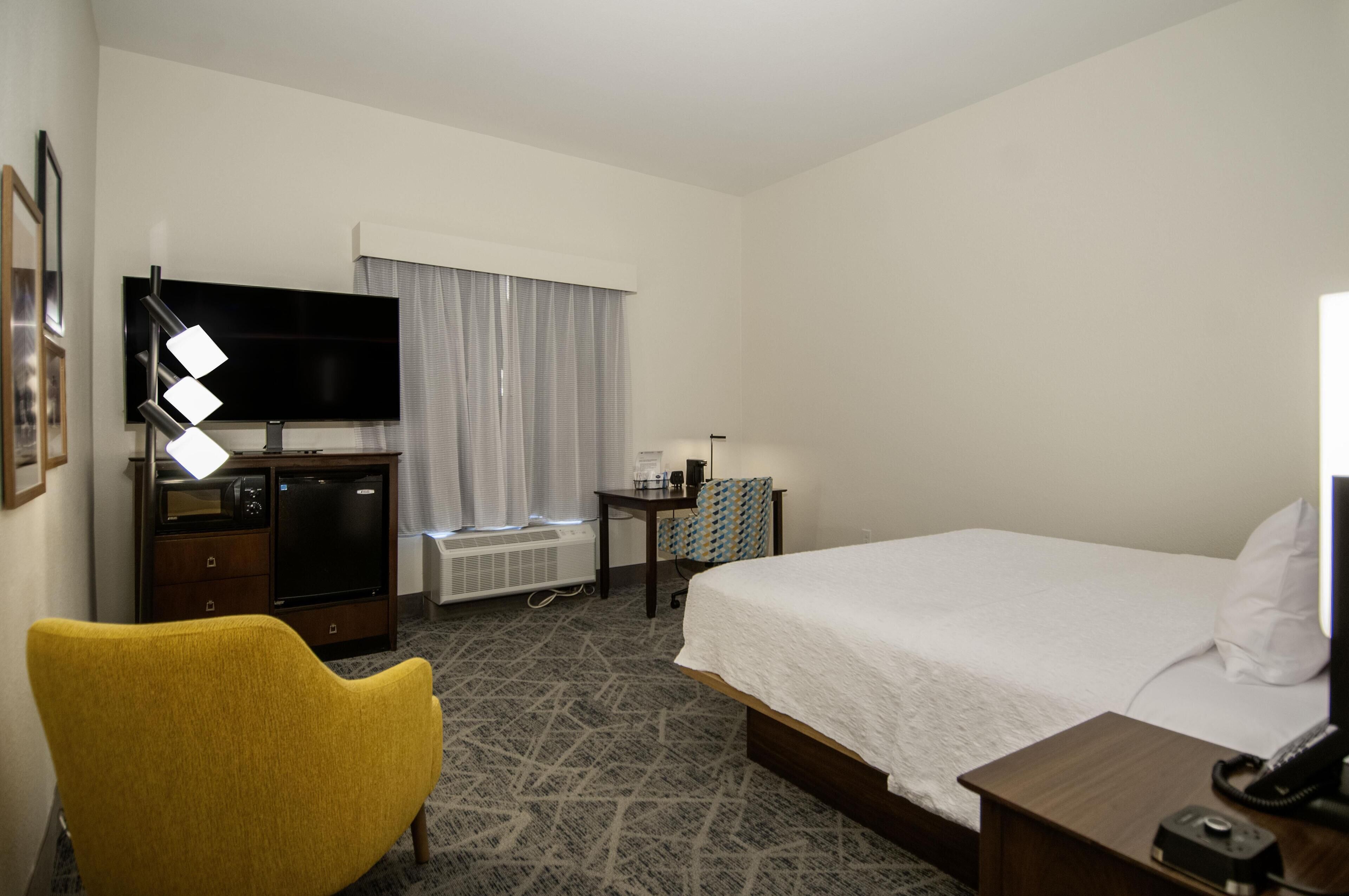 Habitación de hotel con cama, escritorio con teléfono, televisor, silla y ventana con cortinas.