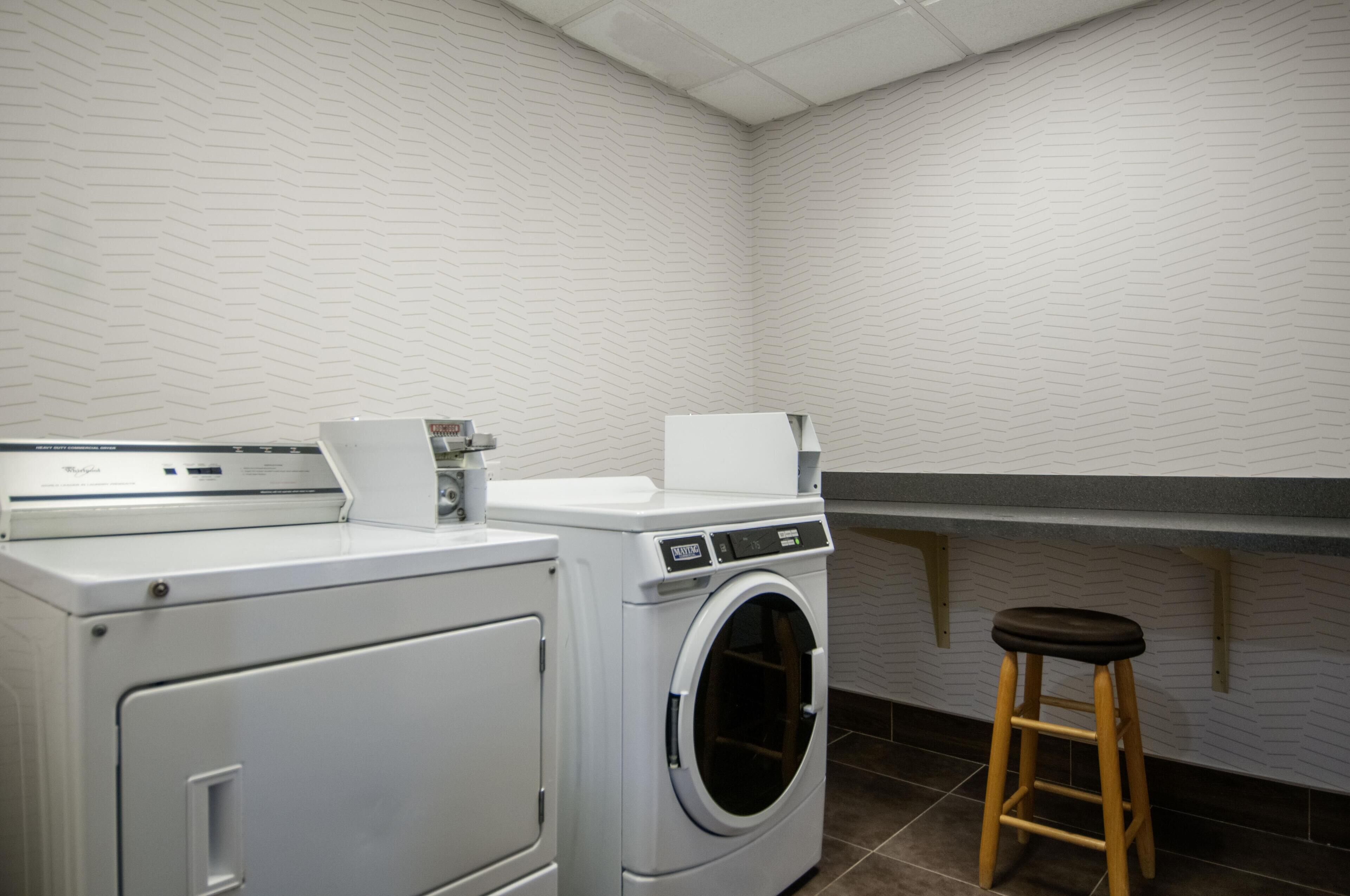 A laundry area with a front-loading washer and dryer, a stool, and a wall-mounted shelf.