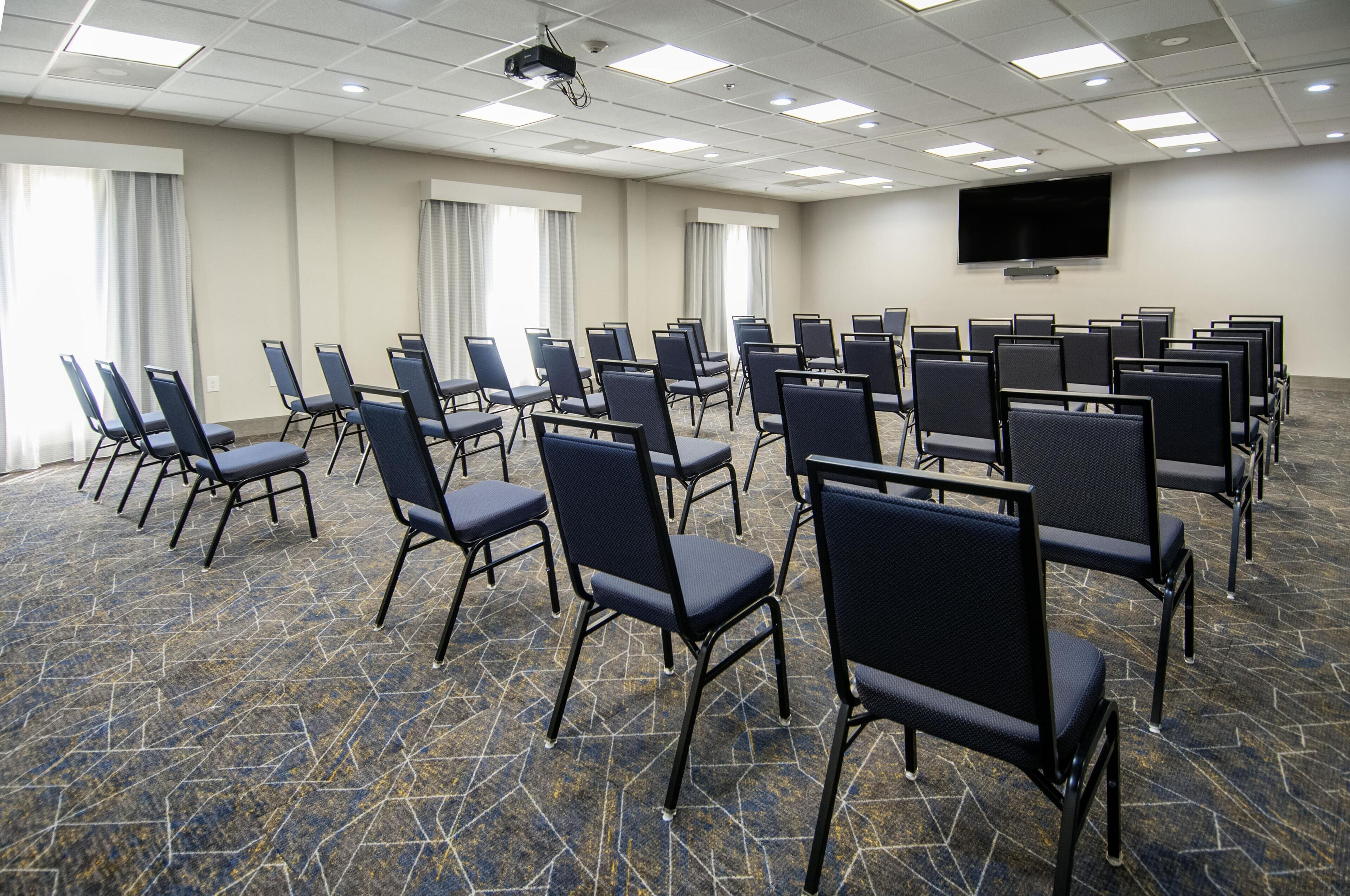 A conference room with rows of chairs, a large screen, and a carpeted floor.
