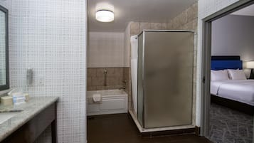 Ein Hotelbad mit Dusche, Badewanne und einem Bett im angrenzenden Zimmer.