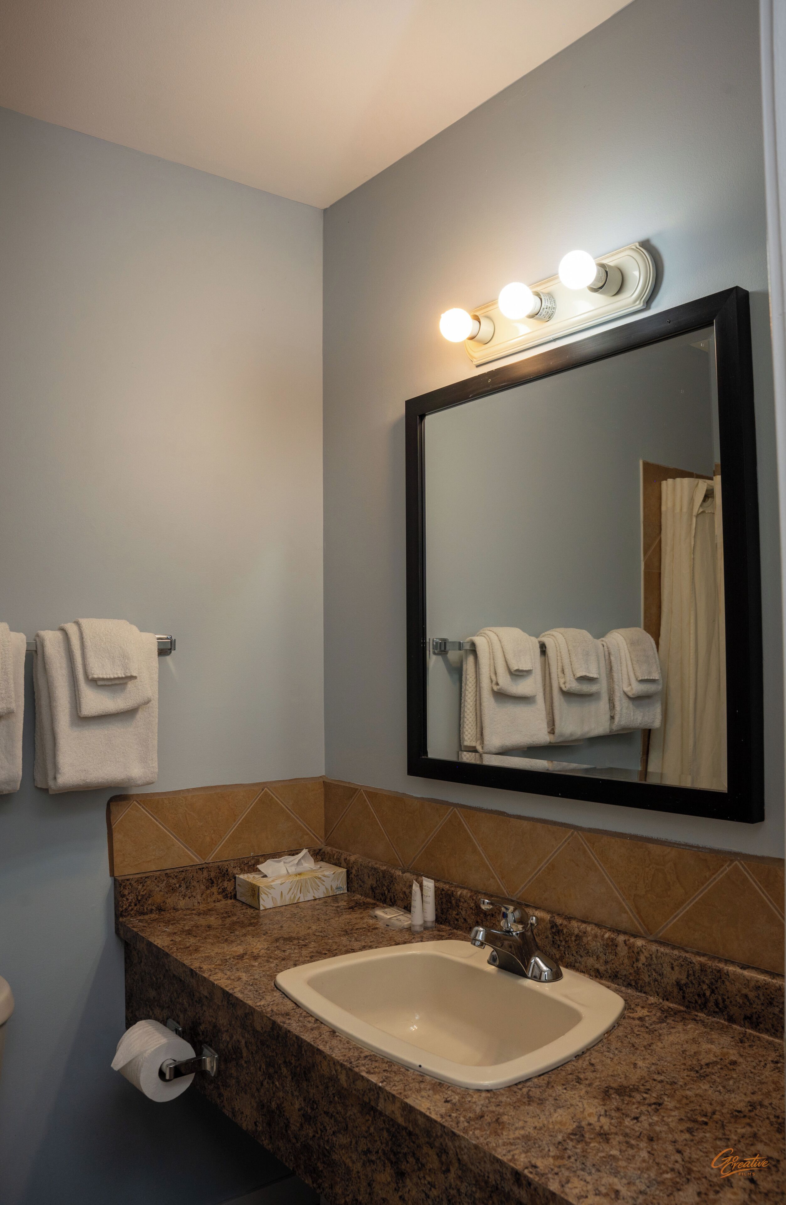 Une salle de bain équipée d’un lavabo, d’un miroir, d’un porte-serviettes et d’un miroir de coiffeuse avec éclairage.