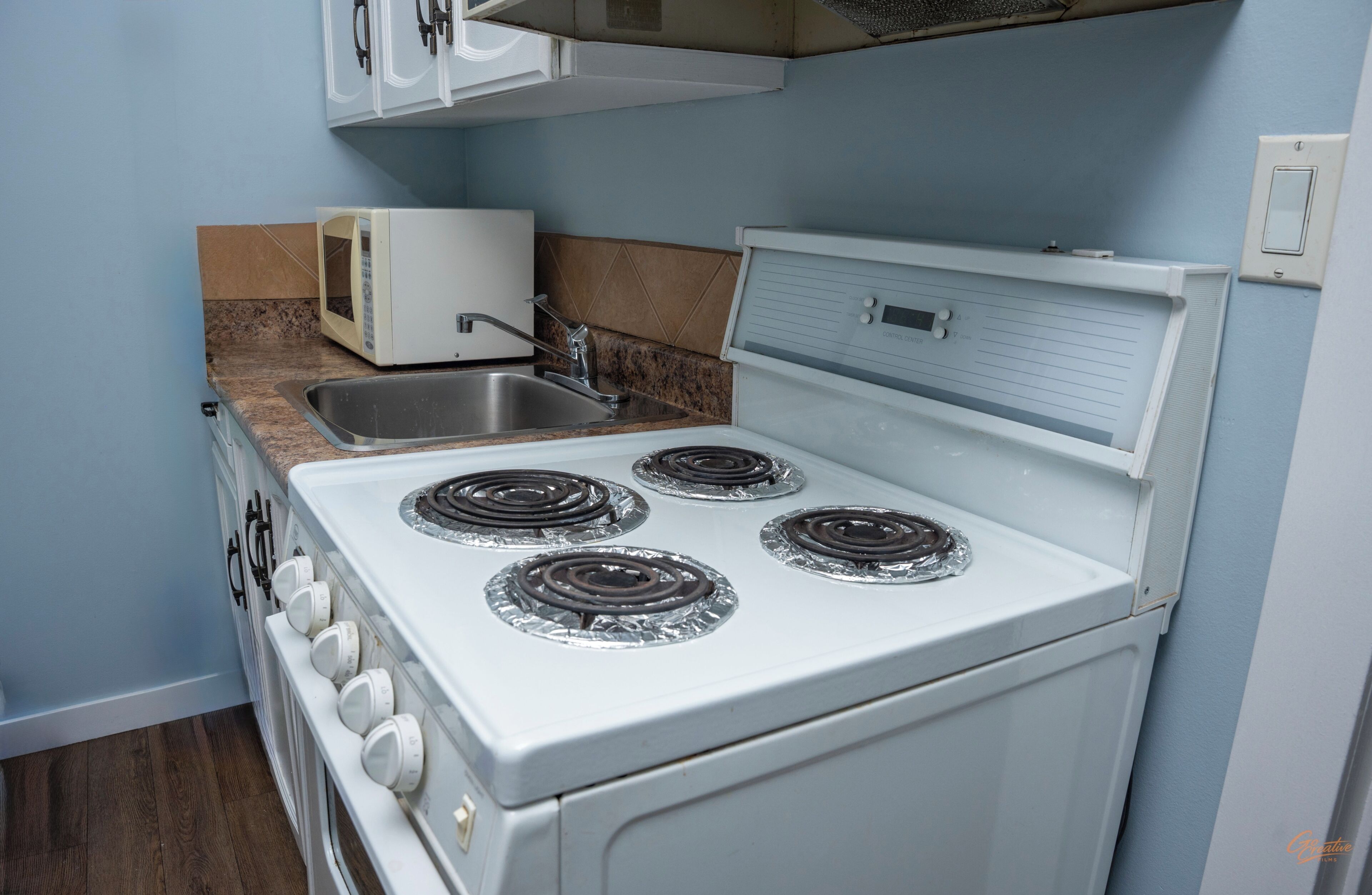 A compact kitchen with a stove, sink, microwave, and a small countertop.