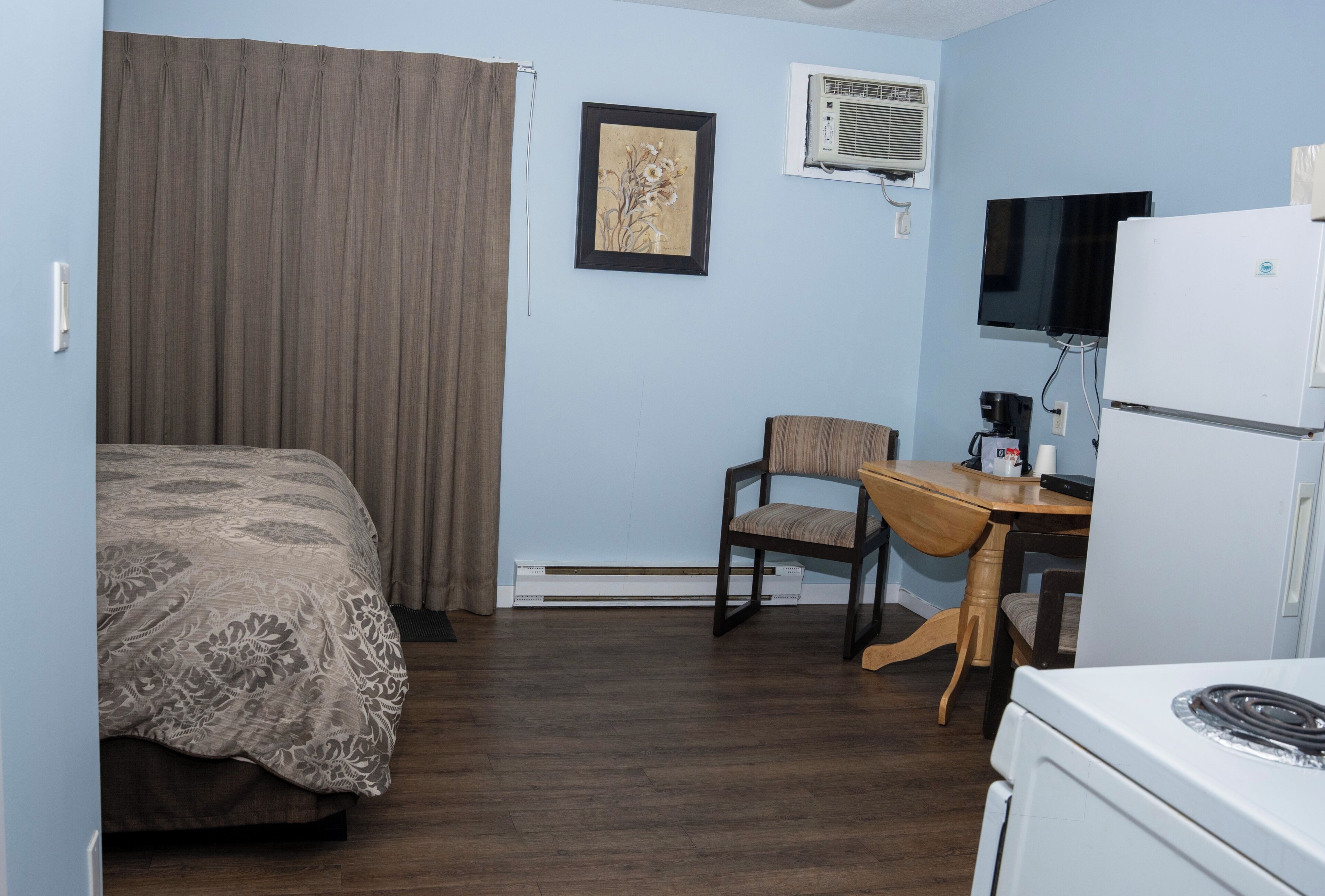 A hotel room with a bed, a desk, a chair, a television, and a refrigerator.