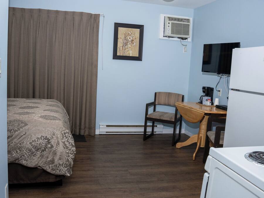 A hotel room with a bed, a desk, a chair, a television, and a refrigerator.