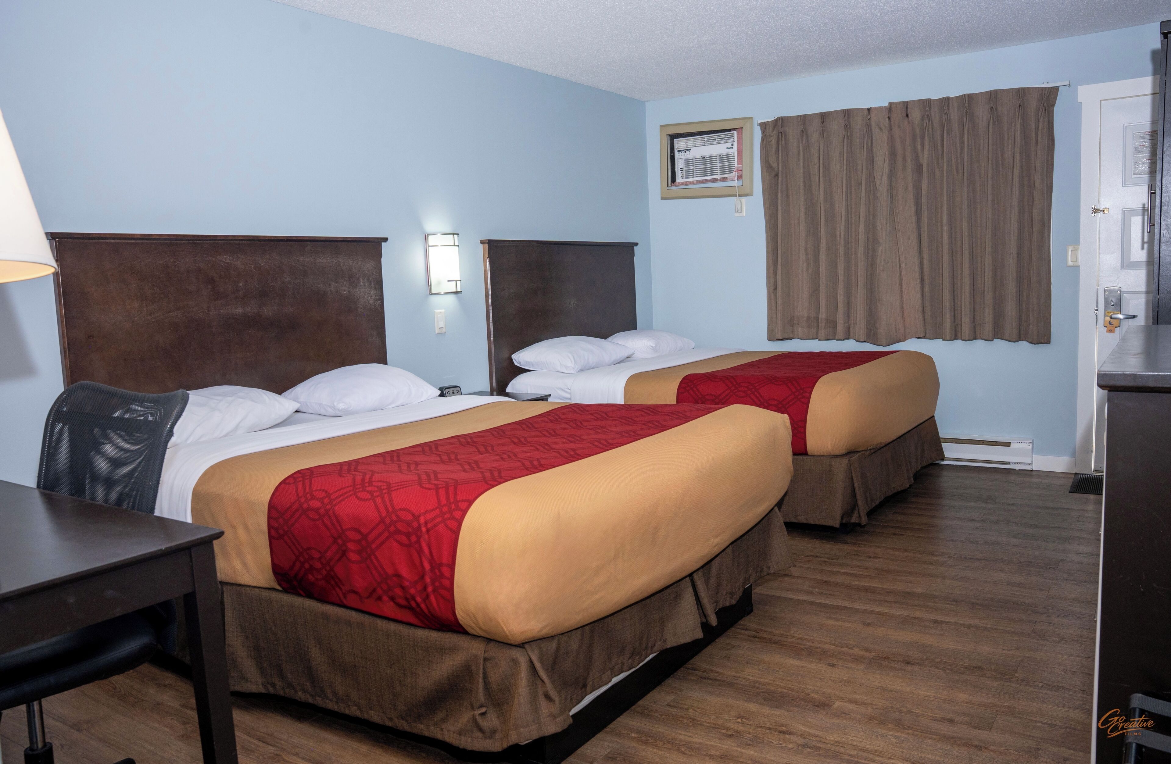 Habitación de hotel con dos camas, un escritorio, una lámpara y una ventana con cortinas.