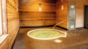 A wooden interior with a hot tub, a door, and a clock on the wall.
