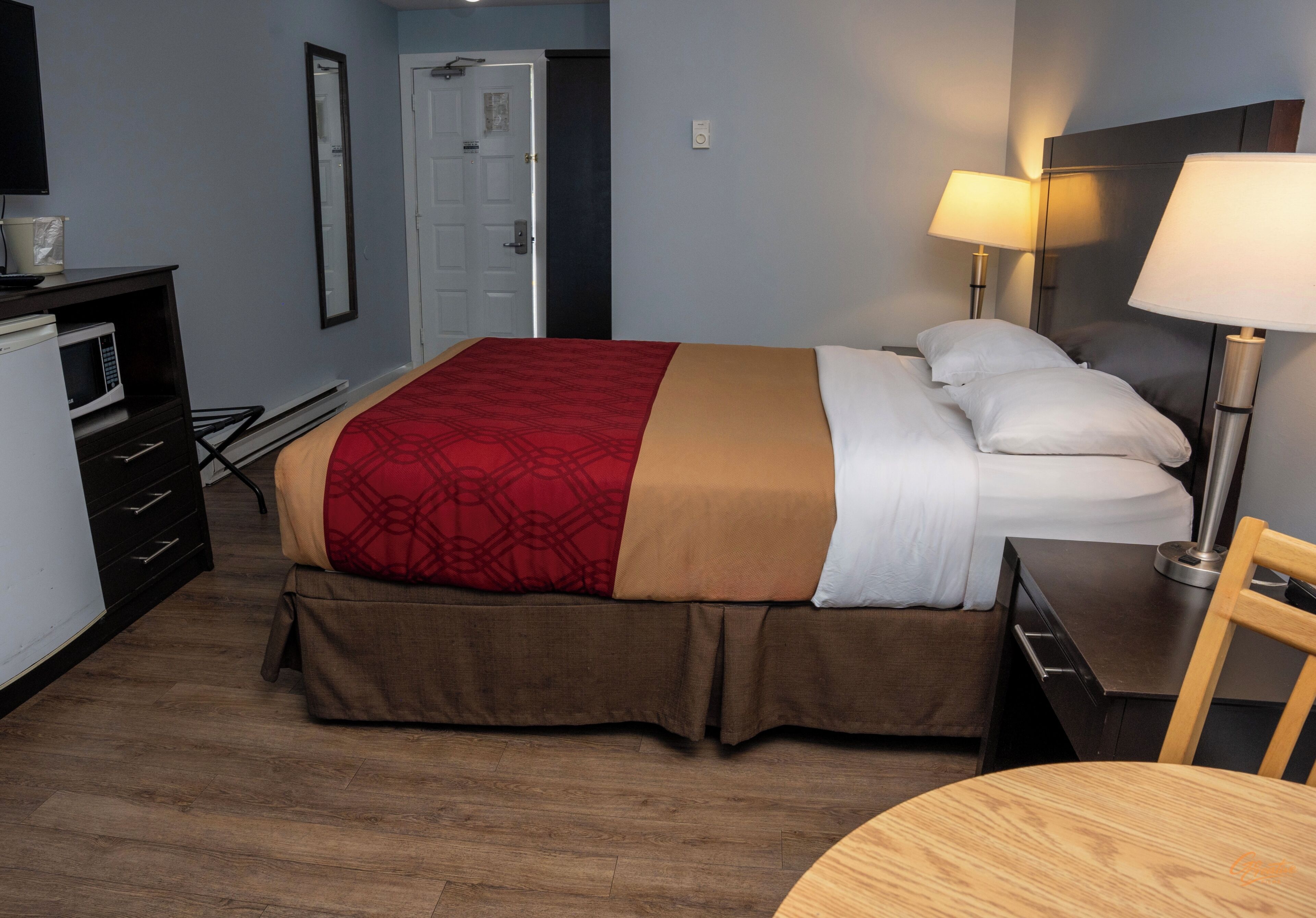 A hotel room with a bed, bedside lamps, a desk, a chair, a microwave, and a wardrobe.