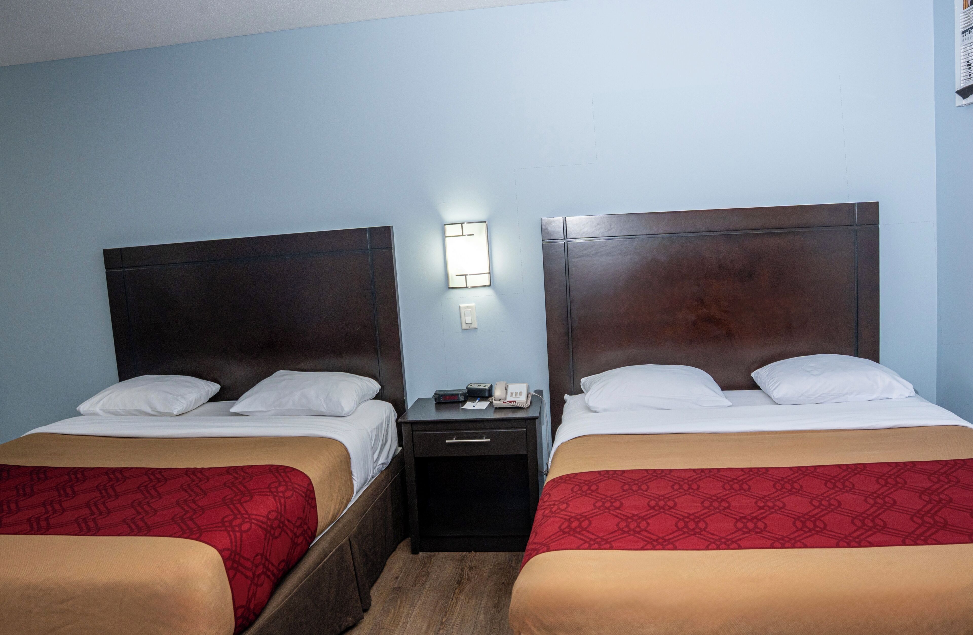 Habitación de hotel con dos camas, una mesita de noche con teléfono y lámpara, y un aplique en la pared.