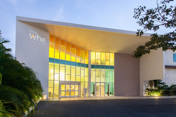 Une entrée d’hôtel moderne avec une façade en verre et une enseigne indiquant « Hôtel WHE BAVARO ».