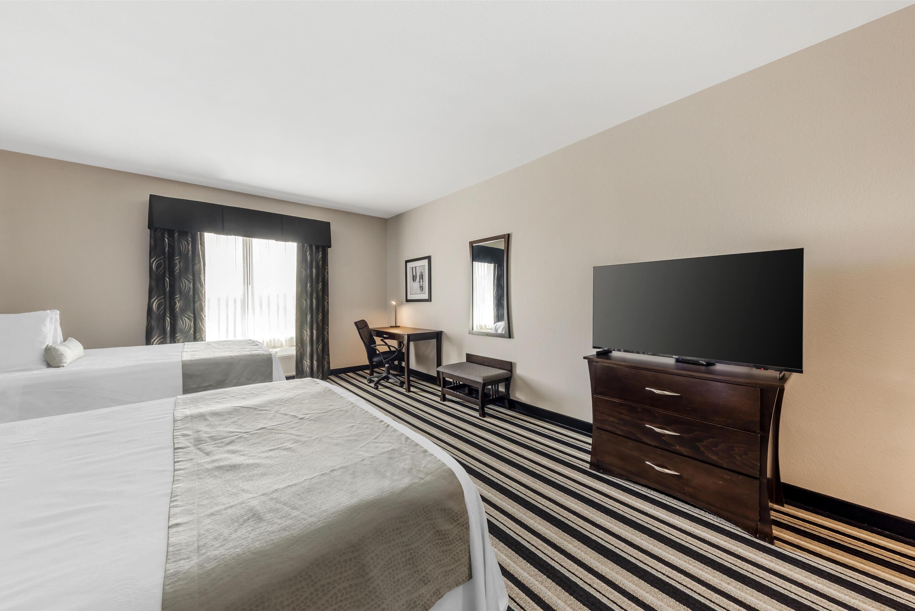 Una habitación de hotel con dos camas, un escritorio, una silla, un televisor y una cómoda.