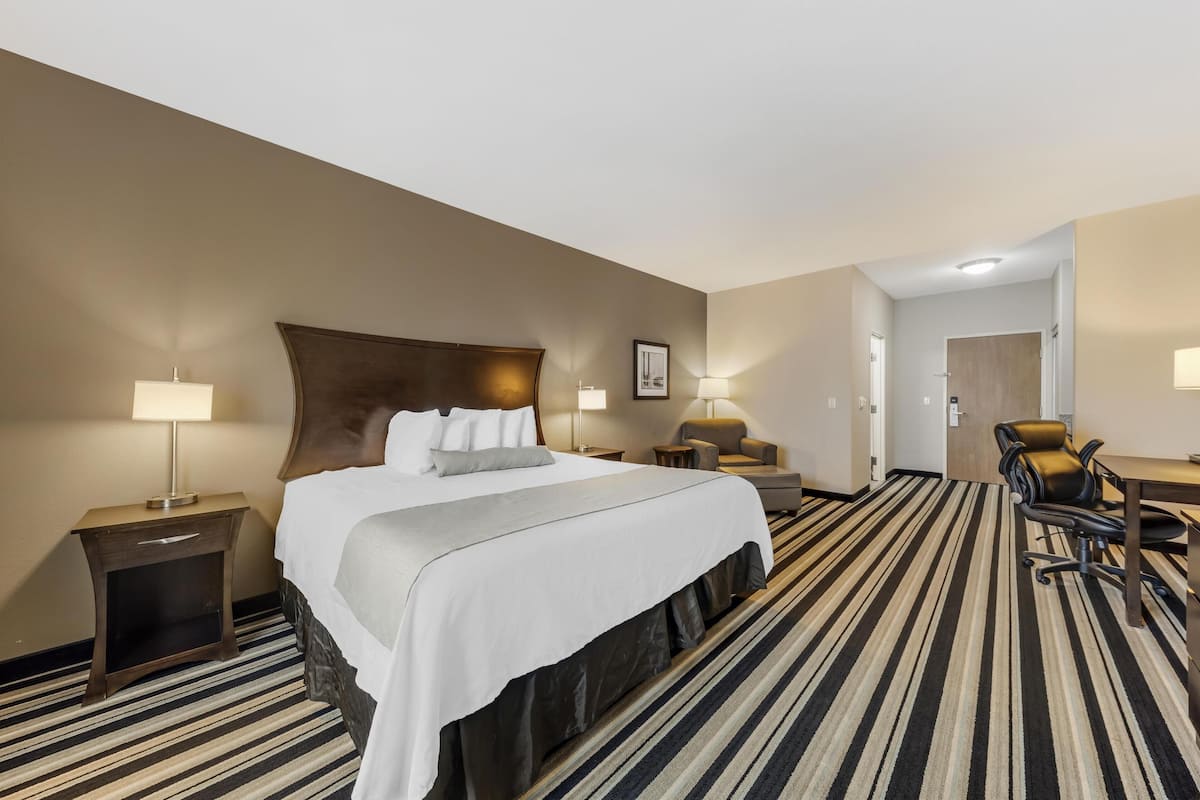 A hotel room with a large bed, two bedside tables with lamps, a desk with a chair, and a striped carpet.