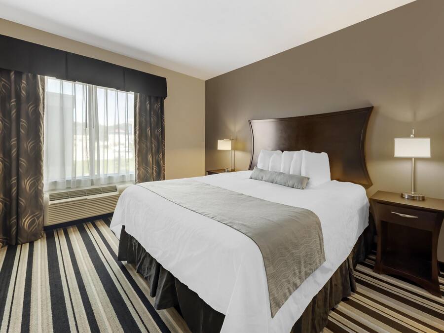 Habitación de hotel con una cama grande, dos lámparas de noche, un ventanal con cortinas y una alfombra a rayas.