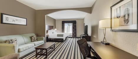 Habitación de hotel con alfombra a rayas, un sofá, una cama, un escritorio y una televisión.