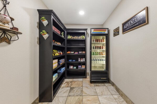 A hallway with a black shelf unit stocked with snacks and a refrigerated display case. - Best Western Plus Sand Bass Inn & Suites (Madill)