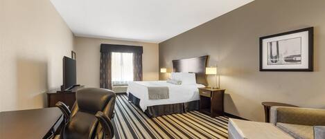 Une chambre d’hôtel avec un lit, un bureau, une chaise, un canapé et un tableau encadré au mur.