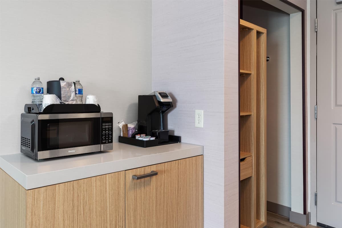 A kitchenette with a microwave, coffee maker, and water bottles on the counter.