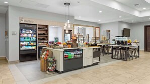 A modern hotel lobby with a reception desk, a chilled beverage fridge, a frozen section, and a coffee bar. - Hilton Garden Inn Auburn (Auburn)