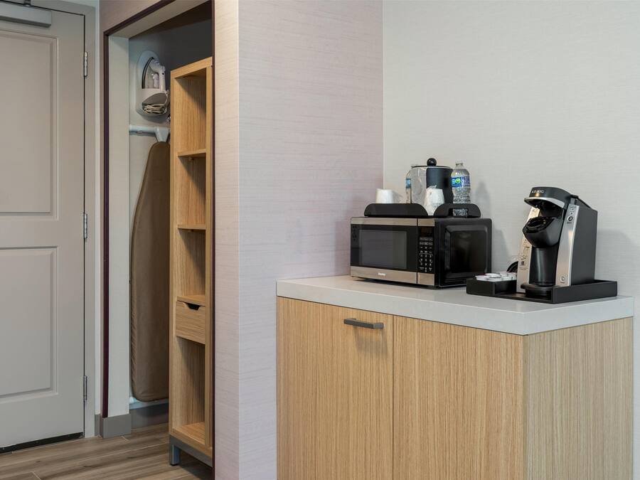 Eine Küchenzeile mit Mikrowelle, Kaffeemaschine und einem kleinen Ablagefach für Toilettenartikel.