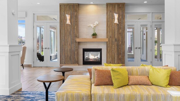 A modern living room with a fireplace, a sofa with cushions, a coffee table, and a chair. - Hilton Garden Inn Auburn (Auburn)