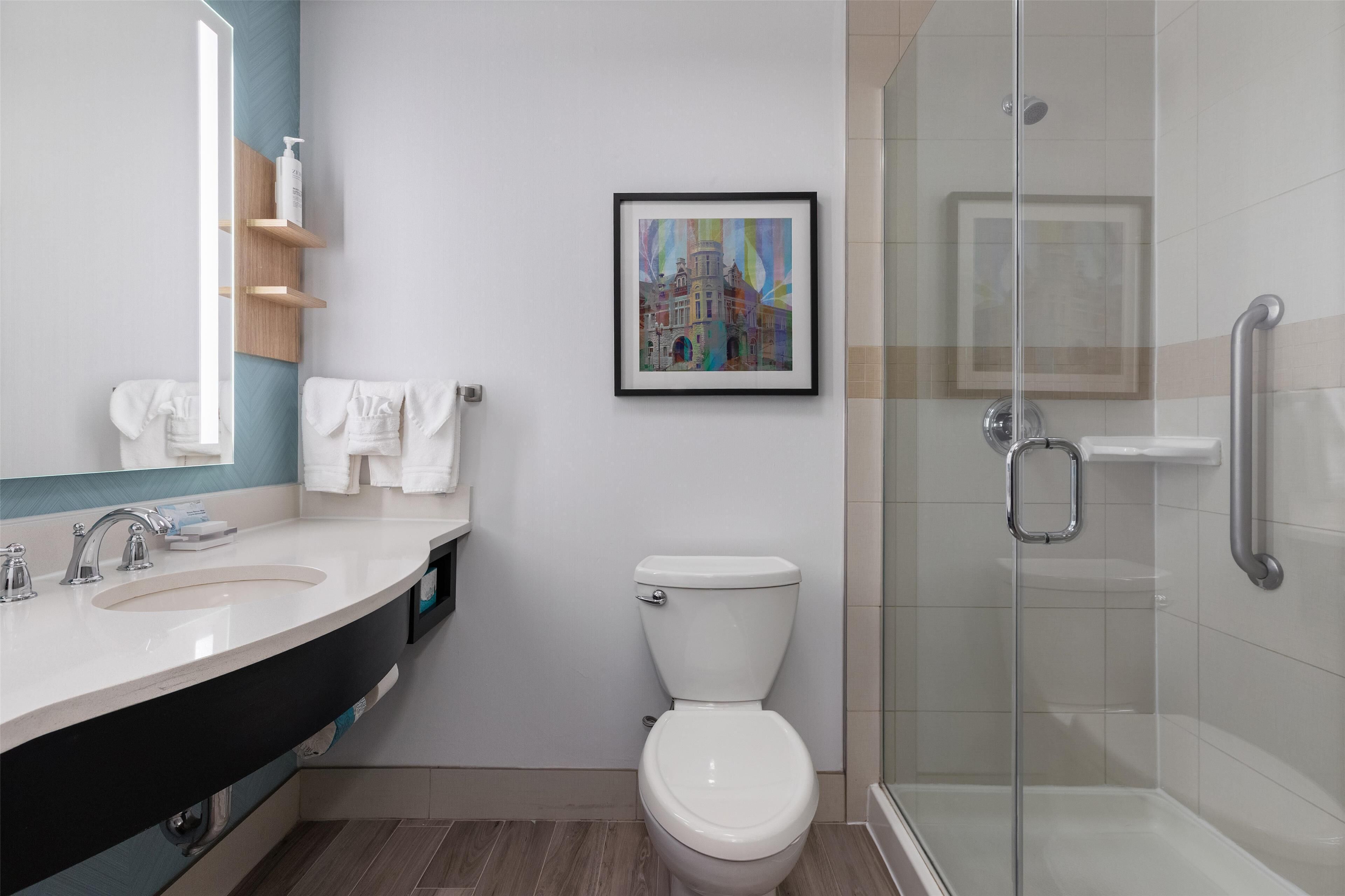 A modern bathroom with a large mirror, two sinks, a toilet, and a glass-enclosed shower.