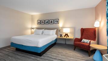 Ett hotellrum med en säng, en stol, ett bord och en väggmonterad lampa.
